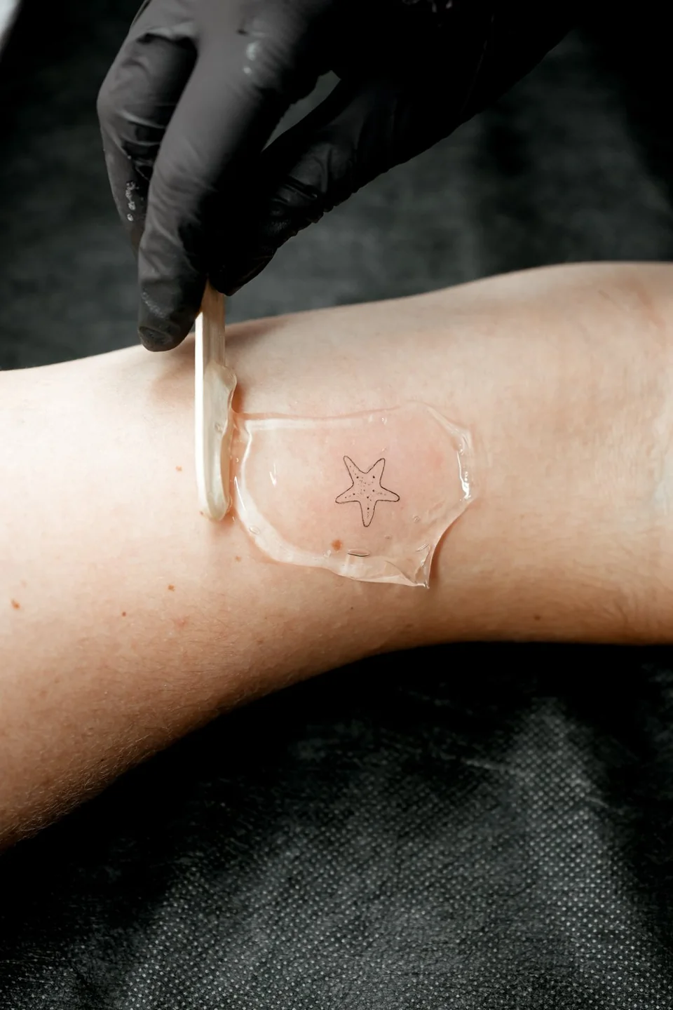 Pequena tatuagem de estrela em linha fina, protegida por uma película transparente.
